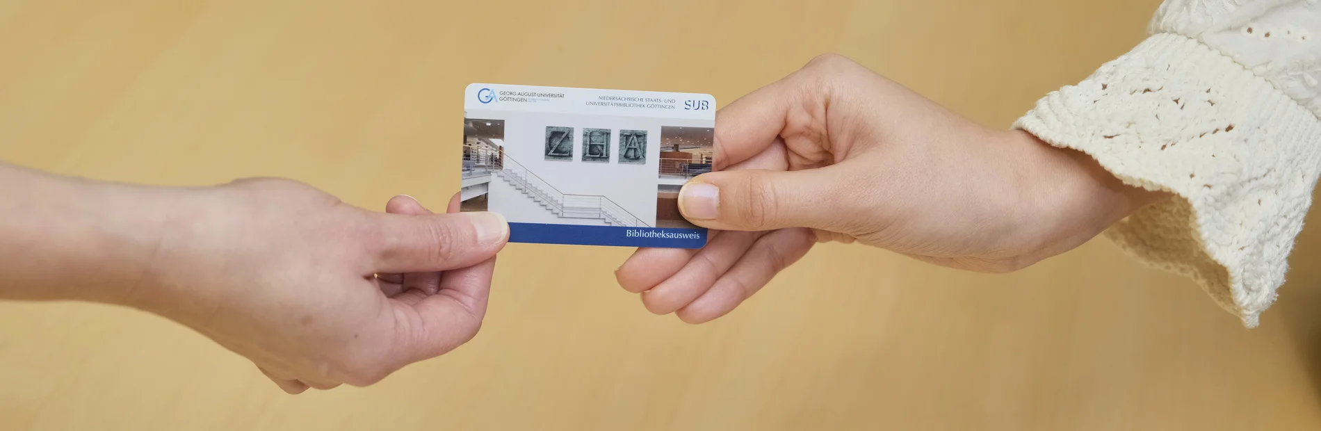 Zwei Hände reichen sich einen Bibliotheksausweis