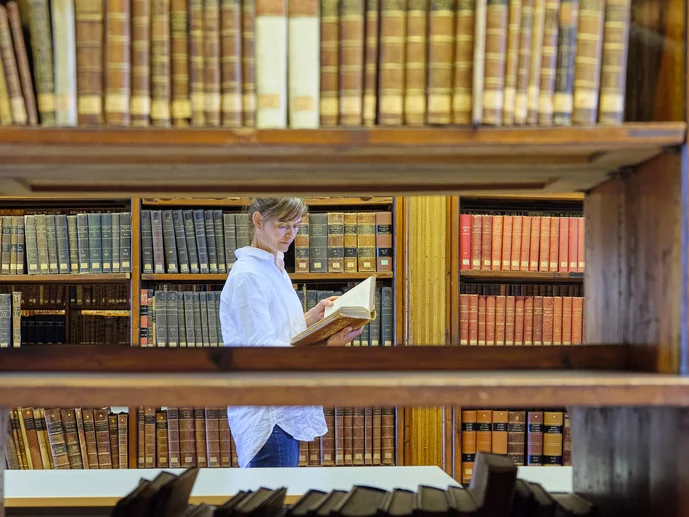 Leserin im Heyne-Saal zwischen Regalen mit alten Büchern, Blick durch ein Bücherregal