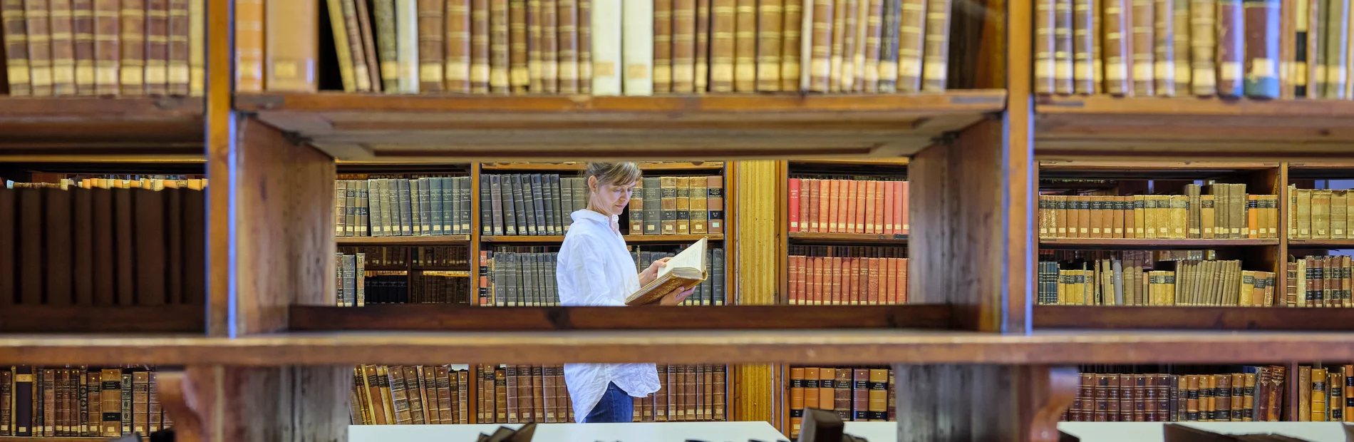 Leserin im Heyne-Saal zwischen Regalen mit alten Büchern, Blick durch ein Bücherregal