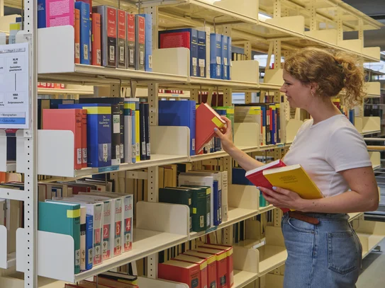 Studentin zieht ein Buch aus einem Regal im Lesesaal der Zentralbibliothek