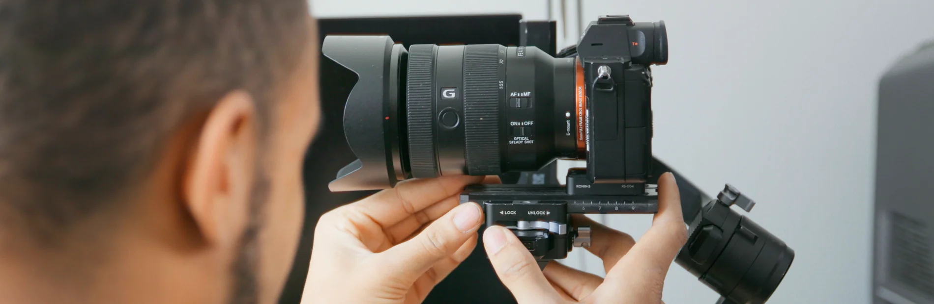 Person justiert eine spiegellose Kamera mit großem Objektiv auf einem Stativ im Innenraum
