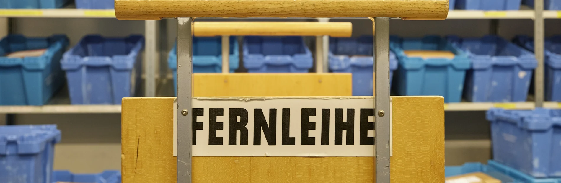 Blaue Kisten im Hintergrund, im Vordergrund ein Bücherwagen mit der Aufschrift Fernleihe
