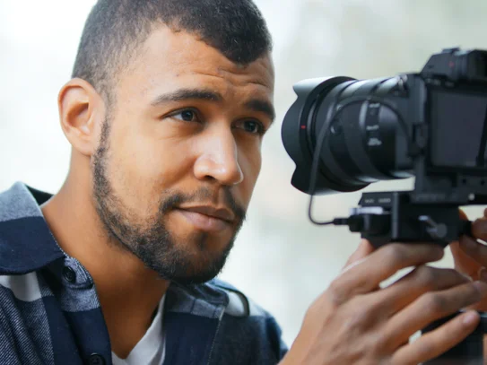 Person hält eine professionelle Kamera mit großem Objektiv auf einem Stabilisator