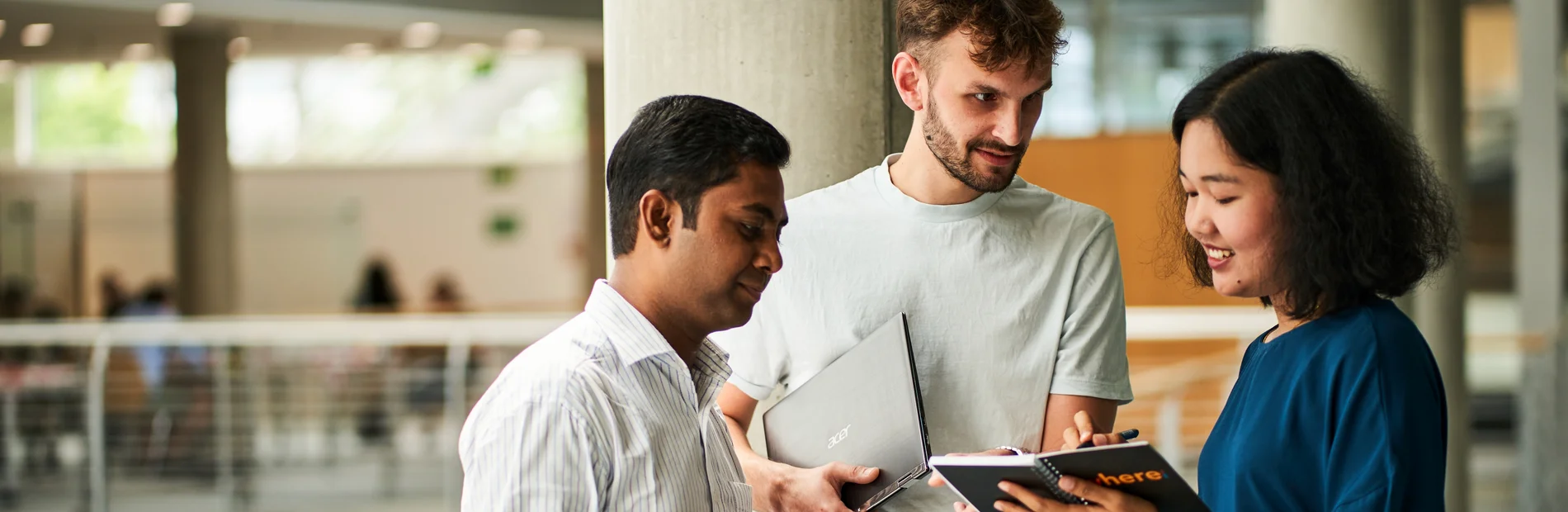 Drei Personen in der Zentralbibliothek. Eine Person hält ein Tablet, eine andere ein Laptop. Die dritte Person hat ein Smartphone in der Hand.