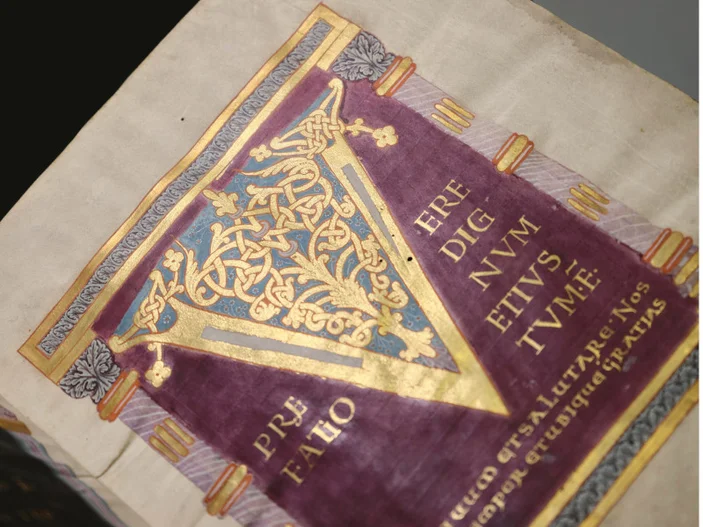 Seite einer mittelalterlichen Handschrift mit rotem Hintergrund und goldener, verzierter V-Initiale