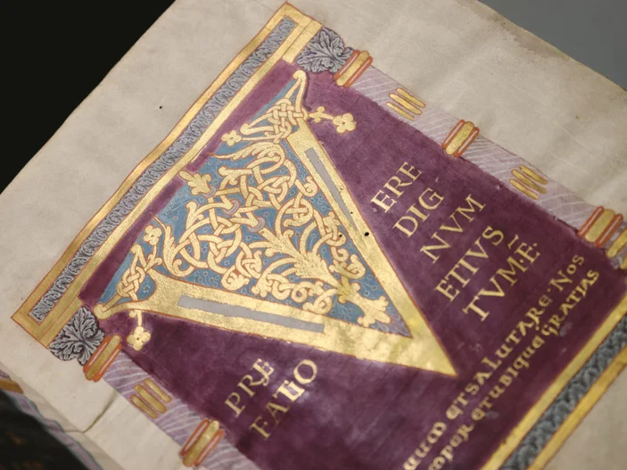 Seite einer mittelalterlichen Handschrift mit rotem Hintergrund und goldener, verzierter V-Initiale