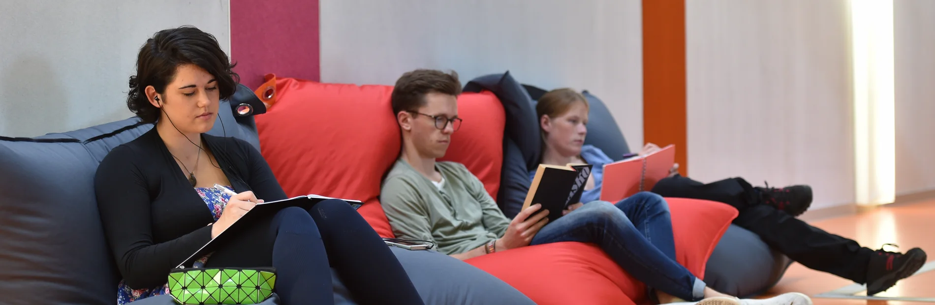 Drei Studierende sitzen auf Sitzsaecken und lesen