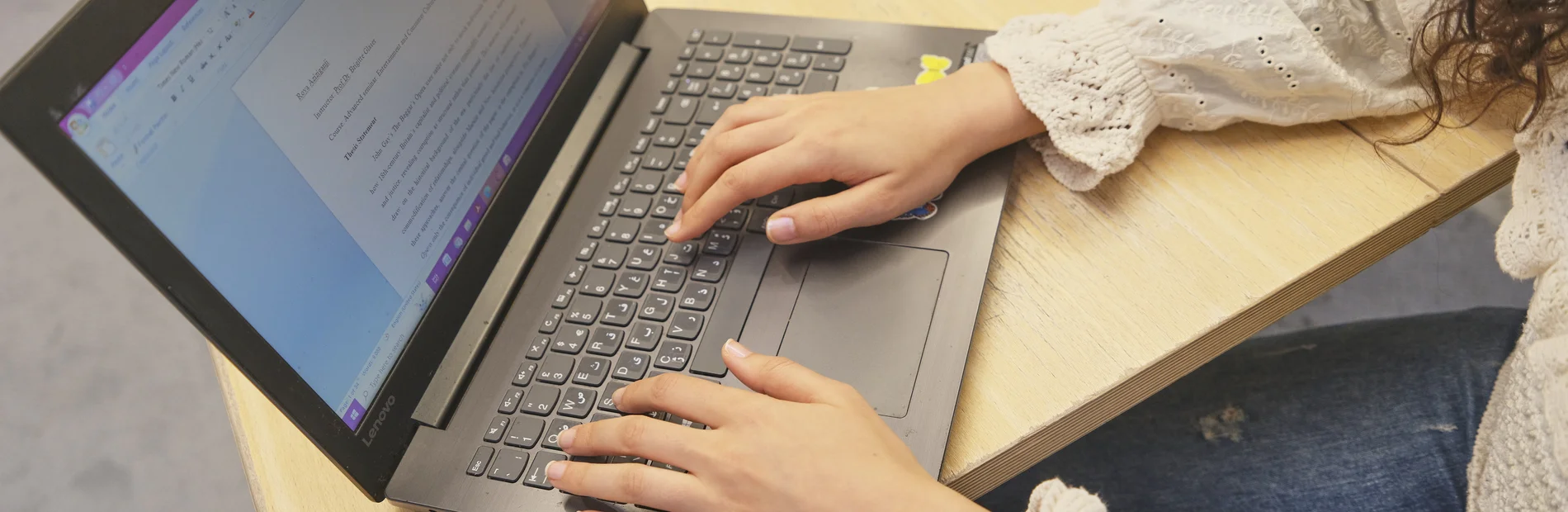 Eine Person arbeitet am Laptop. Auf dem Bildschirm ist eine Textdatei geöffnet.