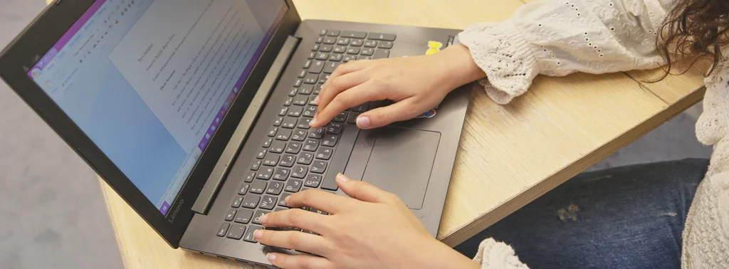 Eine Person arbeitet am Laptop. Auf dem Bildschirm ist eine Textdatei geöffnet.