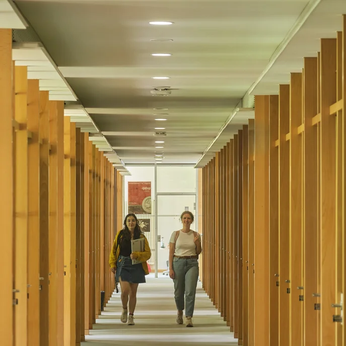 Zwei Studentinnen gehen einen Gang zwischen Arbeitskabinen in der Zentralbibliothek entlang